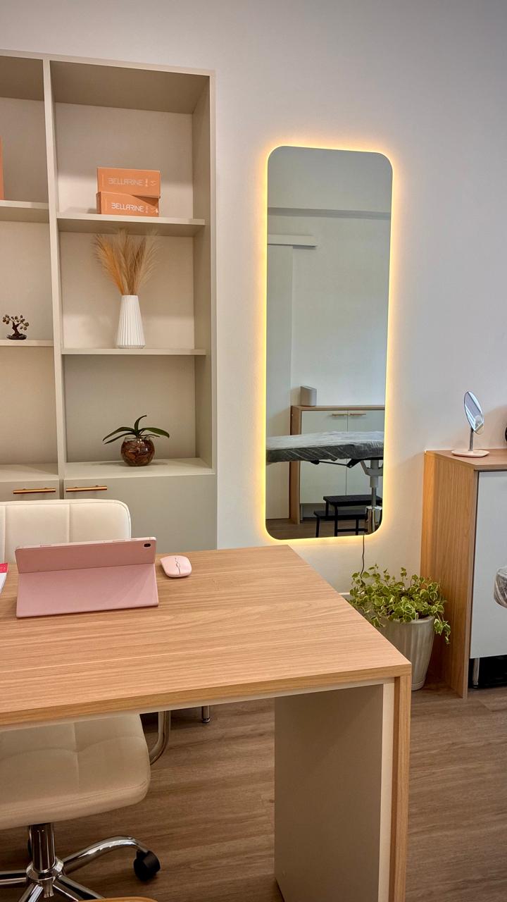 Espaço de atendimento com mesa de avaliação, espelho iluminado e maca ao fundo